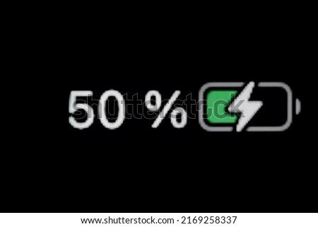 Smartphone charged battery level indicator - charging process - fifty, 50 percent: close up macro view of gadget display, screen, black background. Energy, technology, digital and symbol concept