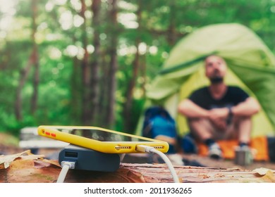 Smartphone is charged using a portable charger. Power Bank charges the phone outdoors with a backpack against the backdrop of a tent and a tourist
