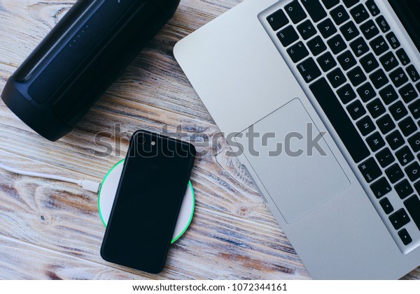 smartphone is charging by wireless charger\
near lapton on wooden\
background