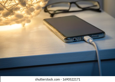 Smartphone charging with energy bank on nightstand at night. Phone Connected to charger