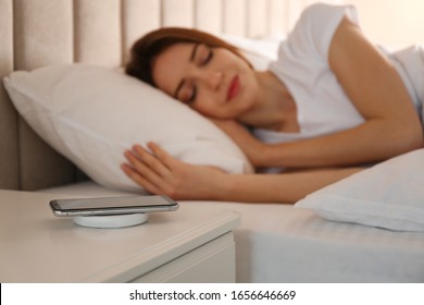 Smartphone charging on wireless pad and woman sleeping in bed