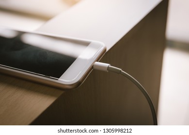 Smartphone charging with power bank on wood table.