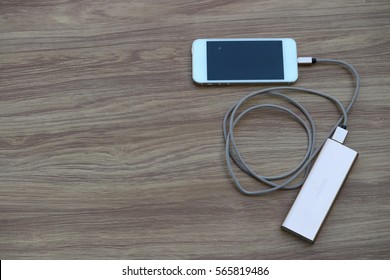 Smartphone charging with power bank on wood background - Shutterstock ID 565819486