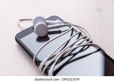 Smartphone With Connected Earphones, White In Color. Earphone Cord Wrapped Around The Phone. Using Earphones To Listen To Music Or To Make Phone Calls.
