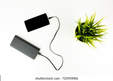 Smartphone Connected To Portable Battery Charger Next To Green Plant On White Background Top View