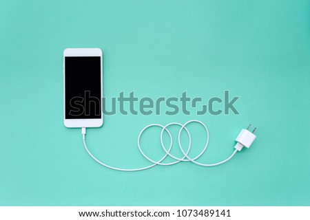 Smartphone Connects to Charger through USB Cable on Turquoise Background Top View
