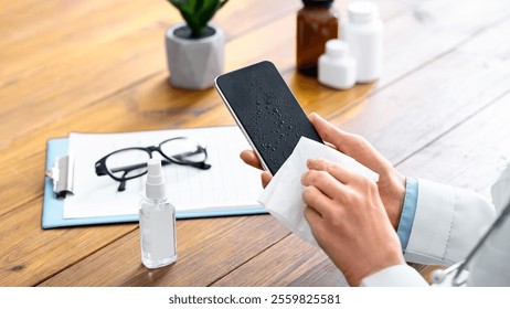 Smartphone disinfection. Female doctor using sanitizer and wipes, cleans phone in office - Powered by Shutterstock