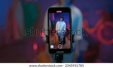 Smartphone display, man vlogger holds clothes on trempels in front of the camera and filming a video for social networks at home. [[stock_photo]] © 