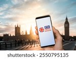 A smartphone displaying the Electronic Travel Authorization or ETA app, held in front of London Big Ben and Parliament. In 2025 all visitors will need an ETA to travel to the UK