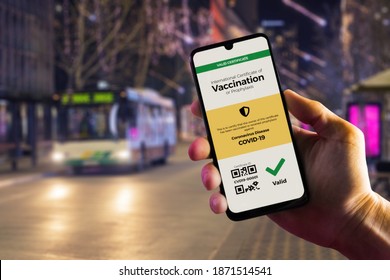 Smartphone displaying a valid digital vaccination certificate for COVID-19 in male's hand, downtown and city bus in background. Vaccination, disease immunity passport, health and surveillance concepts - Shutterstock ID 1871514541