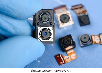 Smartphone Dual Sensor Camera Module In Scientist Hands, With Other Cell Phone Cameras On Background.