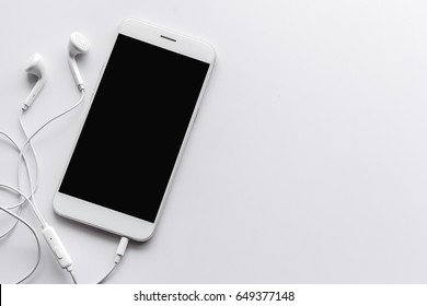 smartphone and earphone on white table with over light in the background