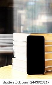 Smartphone with empty screen, next to a stack of books. With copy space. Vertical.