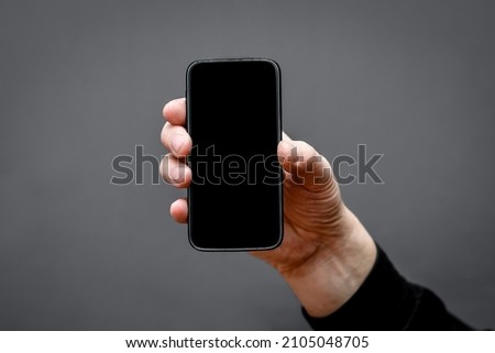  smartphone frame with an empty black screen on a dark background in a man's hand.