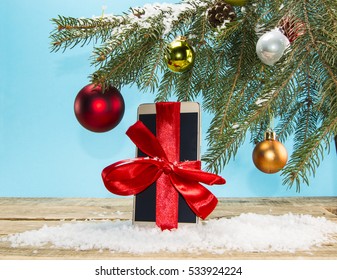 Smartphone gift under the Christmas tree in the snow on a wooden background - Powered by Shutterstock