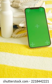 Smartphone With Green Screen, Beach Things, Striped Towel On Background. Sunscreen In White Bottle, Bag. Concept Of Tourism, Online Hotel Booking, Mobile Application, Vacation, Spa. Nobody. Vertical.