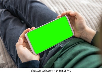 Smartphone with a green screen in hand child . Phone a for keying is holding kid. Smartphone with a hromakey in the hands of a child top view close up.
