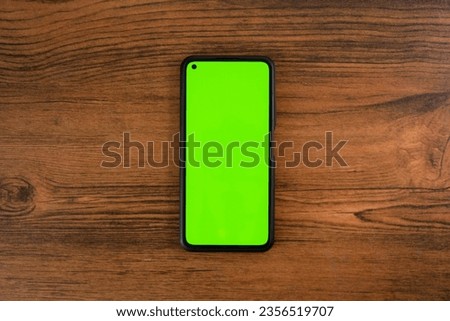 Smartphone with green screen on wooden table.