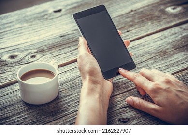 Smartphone in hands on the background of a wooden table and a cup of coffee.