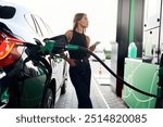 Smartphone in hands. A young woman at a gas station with her car.