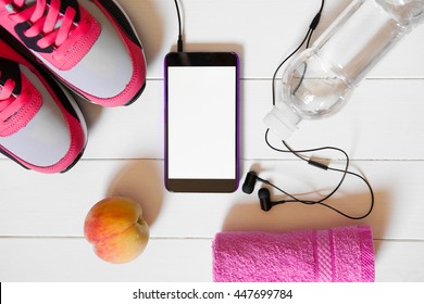 Smartphone With Headphones With Empty Screen And Red Sneakers, Bottle With Water, Towel, Peach On White Wooden Background. Top View, Flat Lay. Mockup Mobile Phone. Sports And Fitness Background.