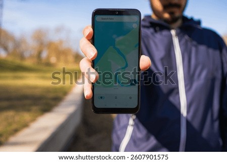 Smartphone with map app shown to camera, man standing on rocky beach near water, navigation, hiking, location search, orientation, outdoor activity, exploring nature, tracking route.
