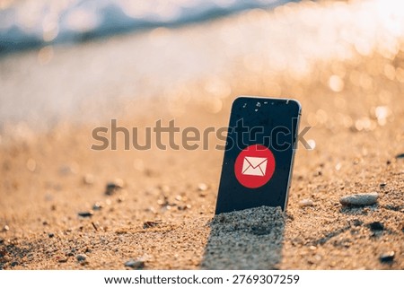 Smartphone with message notification icon stuck in wet sand on a beach at sunset, symbolizing digital communication and vacation Selective focus.