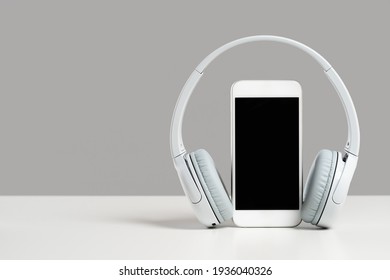 Smartphone Mockup Display With Grey Wireless Headphones On White Desk Gray Background. Copy Space. Audio Technology Apps, Music Podcasts Books