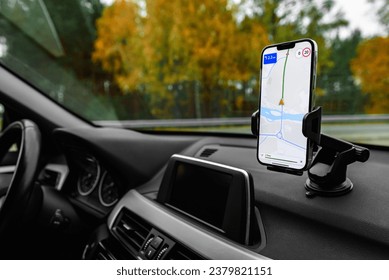 Smartphone with navigation route on screen mounted on phone holder at car dashboard.