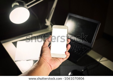 smartphone on hand and desk background.hand holding phone white screen over work table.