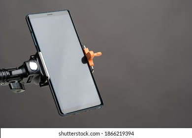 Smartphone on the holder. Smartphone is mounted vertically on the holder. Mobile phone on a gray background. Smartphone with a clear screen. Phone next to the text location. Technical gadgets.