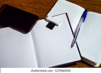 smartphone on an open diary with a ballpoint pen and a flash drive on the table