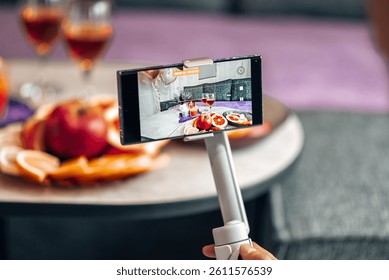 A smartphone on a stabilizer records a beautifully set table with vibrant fruits and wine, creating cinematic content for digital storytelling.