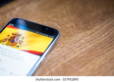Smartphone on wooden background with 5G network sign 25 per cent charge and Spain flag on the screen.
