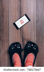 Smartphone On Wooden Wooden Floor. Black Friday Advert. Woman Feet In Cat Slippers, Striped Socks. Top View. Online Shopping Concept.