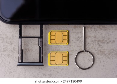 smartphone and open slots for micro SD and nano SIM cards, two nano SIM cards and metal key on grey background top view