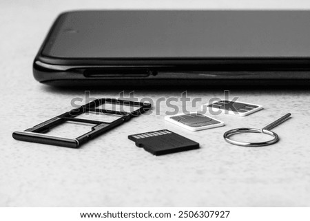 smartphone with open slots for micro SD and nano SIM cards, two nano SIM cards and metal key on grey background black white photo