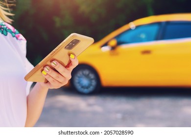 Smartphone or phone in female hands on a blurred background of a yellow taxi service car. Car call and control in the application. - Powered by Shutterstock