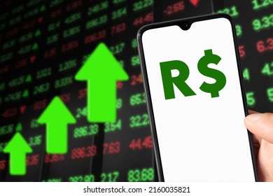 Smartphone With Real (R$) Symbol And Background Showing Market Value Rising.