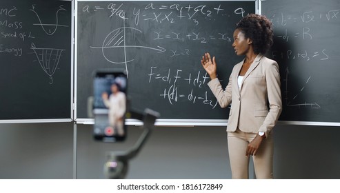 Smartphone recording video lesson at school. African American young female teacher explaining math or physics formulas at class. Online studying. 