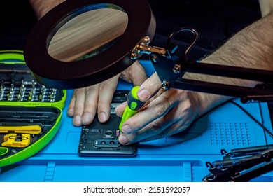 Smartphone Repair In A Service Center. Hands Of A Professional Master Repairman Repairing Disassembled Into Pieces Cell Phone. Internal Parts, Chips, Motherboards, Wiring, Fixing Process.