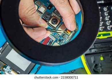 Smartphone Repair In A Service Center. Hands Of A Professional Master Repairman Repairing Disassembled Into Pieces Cell Phone. Internal Parts, Chips, Motherboards, Wiring, Fixing Process.