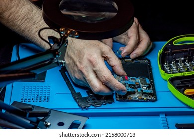 Smartphone Repair In A Service Center. Hands Of A Professional Master Repairman Repairing Disassembled Into Pieces Cell Phone. Internal Parts, Chips, Motherboards, Wiring, Fixing Process.