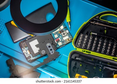 Smartphone Repair In A Service Center. Hands Of A Professional Master Repairman Repairing Disassembled Into Pieces Cell Phone. Internal Parts, Chips, Motherboards, Wiring, Fixing Process.