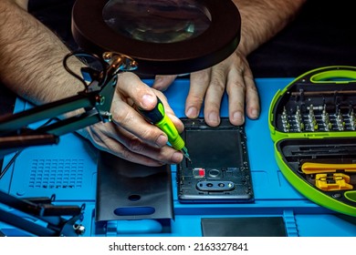 Smartphone Repair In A Service Center. Hands Of A Professional Master Repairman Repairing Disassembled Into Pieces Cell Phone. Internal Parts, Chips, Motherboards, Wiring, Fixing Process.