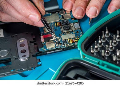 Smartphone Repair In A Service Center. Hands Of A Professional Master Repairman Repairing Disassembled Into Pieces Cell Phone. Internal Parts, Chips, Motherboards, Wiring, Fixing Process.