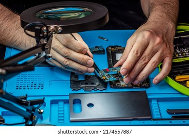 Smartphone Repair In A Service Center. Hands Of A Professional Master Repairman Repairing Disassembled Into Pieces Cell Phone. Internal Parts, Chips, Motherboards, Wiring, Fixing Process.