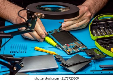 Smartphone Repair In A Service Center. Hands Of A Professional Master Repairman Repairing Disassembled Into Pieces Cell Phone. Internal Parts, Chips, Motherboards, Wiring, Fixing Process.