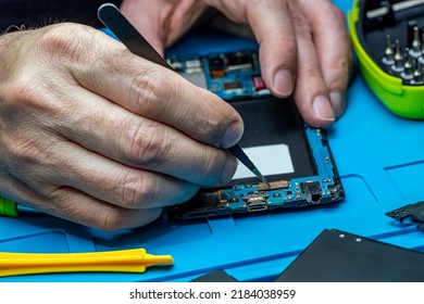 Smartphone Repair In A Service Center. Hands Of A Professional Master Repairman Repairing Disassembled Into Pieces Cell Phone. Internal Parts, Chips, Motherboards, Wiring, Fixing Process.