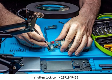 Smartphone Repair In A Service Center. Hands Of A Professional Master Repairman Repairing Disassembled Into Pieces Cell Phone. Internal Parts, Chips, Motherboards, Wiring, Fixing Process.